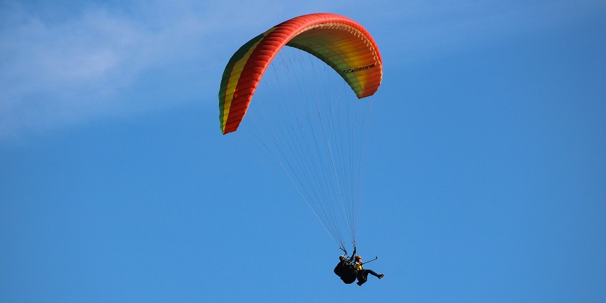 A person in a yellow parachute glides through a clear blue sky on a sunny day