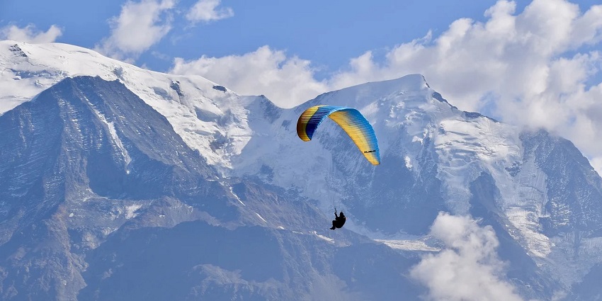 Distant view of a tourist paragliding with snow caped majestic ranges in the backdrop