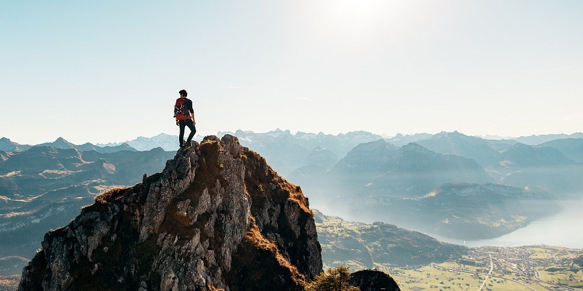 A man stands on a rock, gazing at the scenic view of Parasnath Hill in the distance.