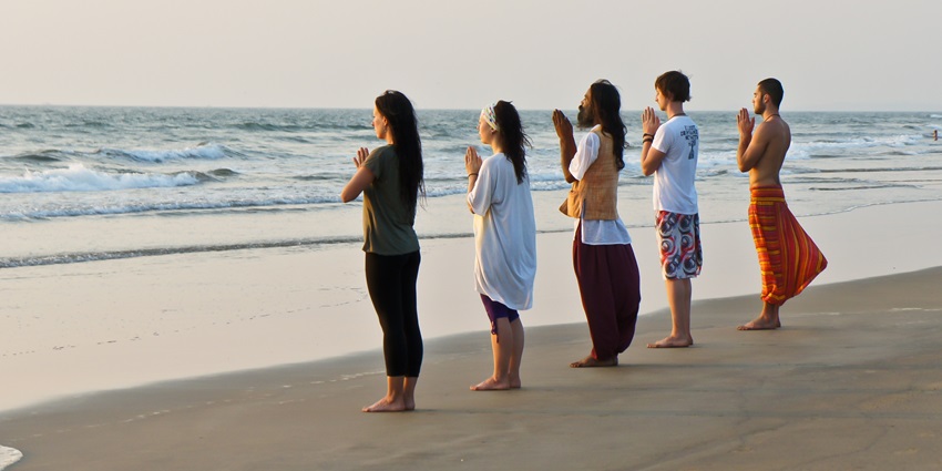 Yoga master and his international students meditate at sunset on the Goa beach, India
