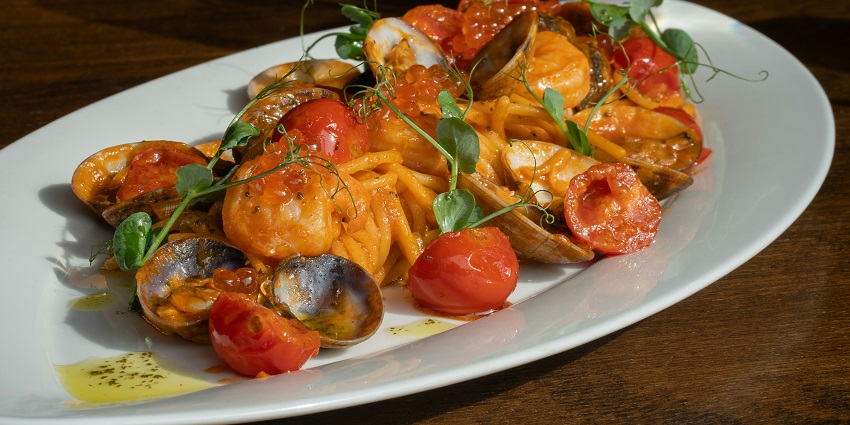 A white plate filled with colourful pasta and fresh vegetables, beautifully arranged.