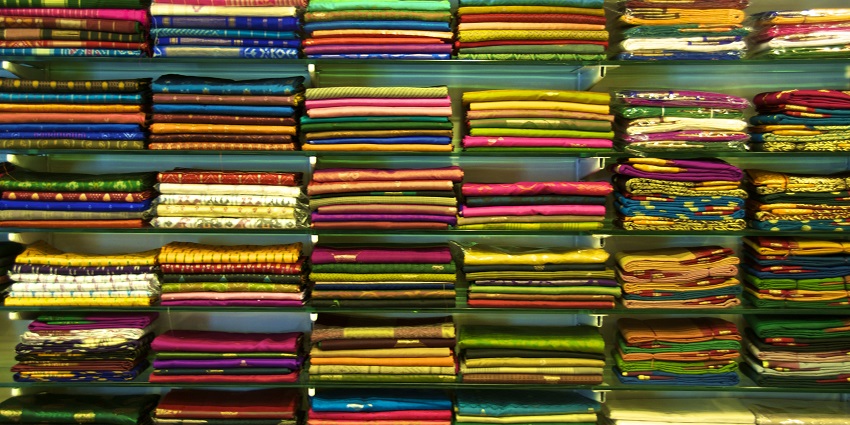 A mindblowing view of a saree shop with multiple colourful fabrics displayed on a shelf.