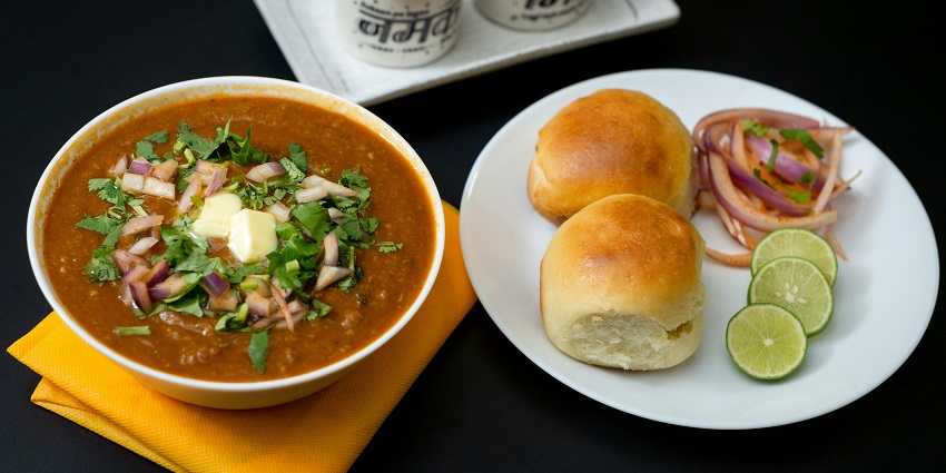 Pav Bhaji dish served on plate and garnished with loads of butter, onion and lemon.
