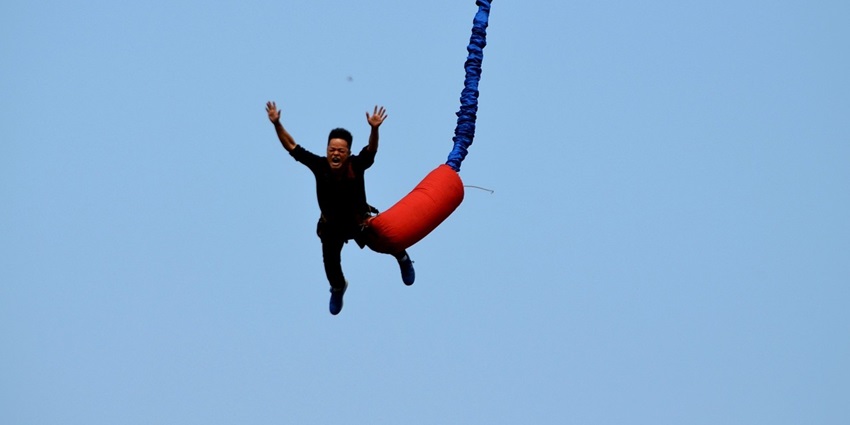 A person bungee jumping off a platform, with the bungee cord stretched out and a panoramic view of the landscape below.