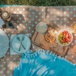 Image of a picnic set up on a green grass field with decorative items, food and drinks