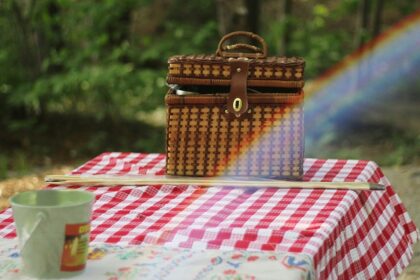 A picnic basket filled with food sits on a wooden table outdoors, inviting a meal