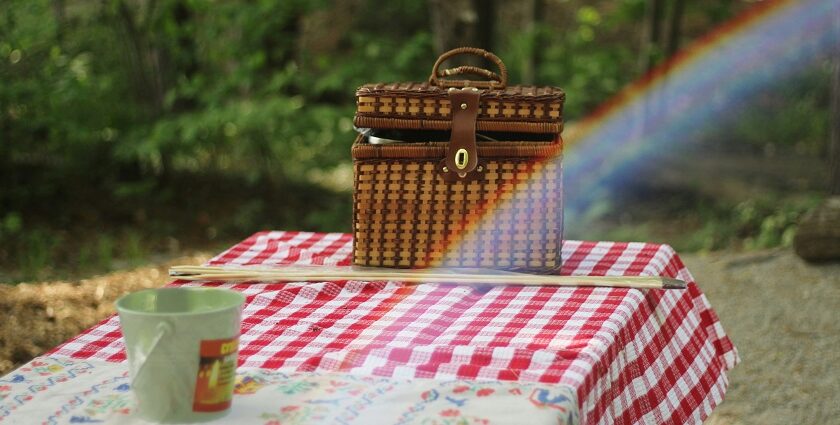 A picnic basket filled with food sits on a wooden table outdoors, inviting a meal