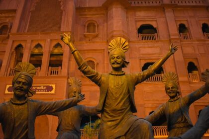 A view of sculptures doing bhangra in front of a majestic tourist attraction in Punjab.