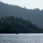 Image of lake surrounded by lush green hills and people on boat ride - Places to Visit Near Panchkula