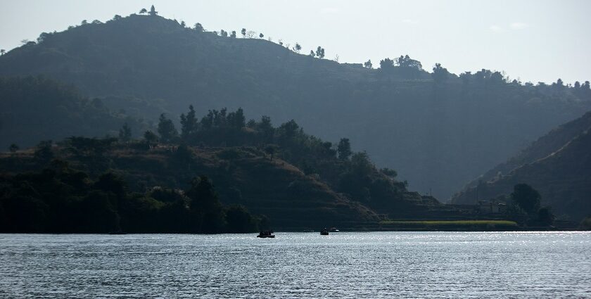 Image of lake surrounded by lush green hills and people on boat ride - Places to Visit Near Panchkula