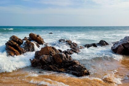 A view of a brown rocky shore at one of the beaches under blue sky during daytime.