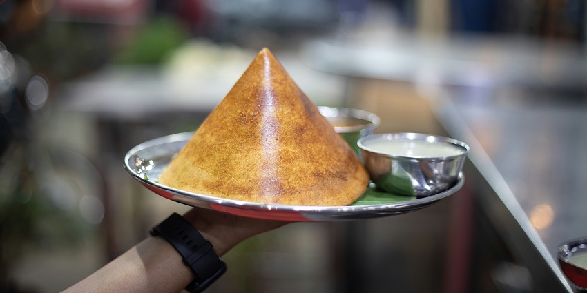 A person holds a plate with a cone-shaped Dosa, showcasing a delightful treat.