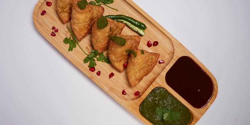 Image of deep fried Samosa - one of the best Indian snacks served on a wooden plate.