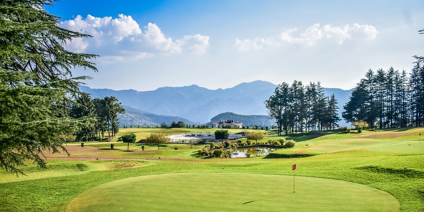 Scenic view of a vast golf course with forested hills in the backdrop
