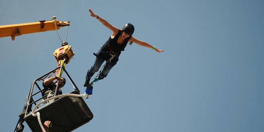 Bungee jumper leaping over the Seti River with a mountain backdrop in Pokhara, Nepal.
