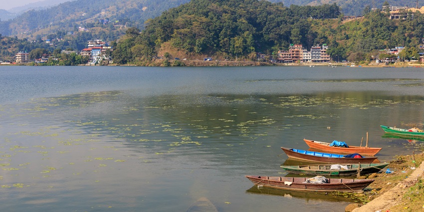A breathtaking view of a lake in Pokhara surrounded by lush green mountains and hills.