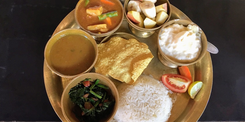 A lip-smacking view of a Nepali thali with dal bhat, fruits and a slice of tomato.