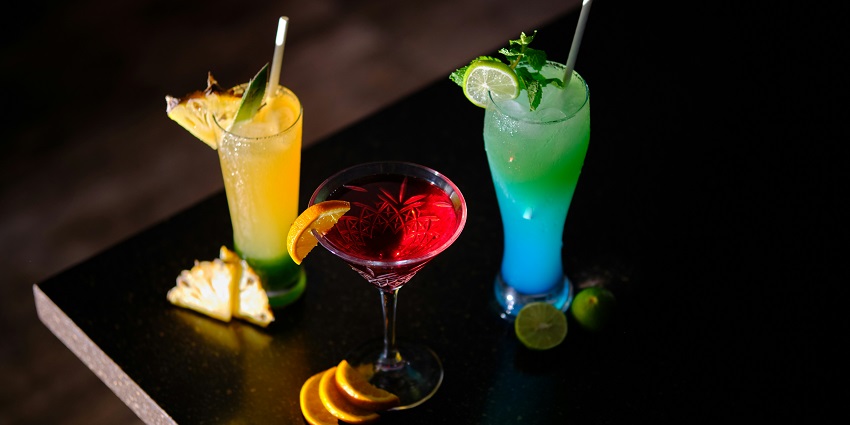 A table featuring three types of drinks: a vibrant cocktail, a fizzy soda, and a fresh juice