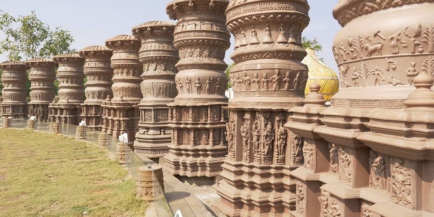 Various engraved pillars are situated in a lush garden with lights under the pillar