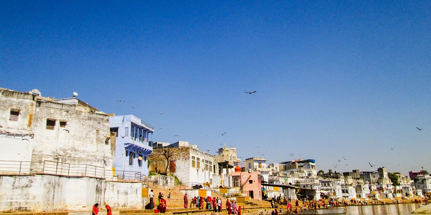 A paraglider soars over Pushkar Lake, Aravalli Hills, temples, and vibrant ghats.
