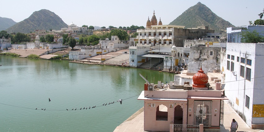 View of Pushkar Lake surrounded by hills with visitors walking along the ghats