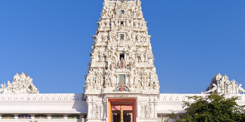 A frontal view of the entrance of a temple in Pushkar with white marble exterior and lush surroundings