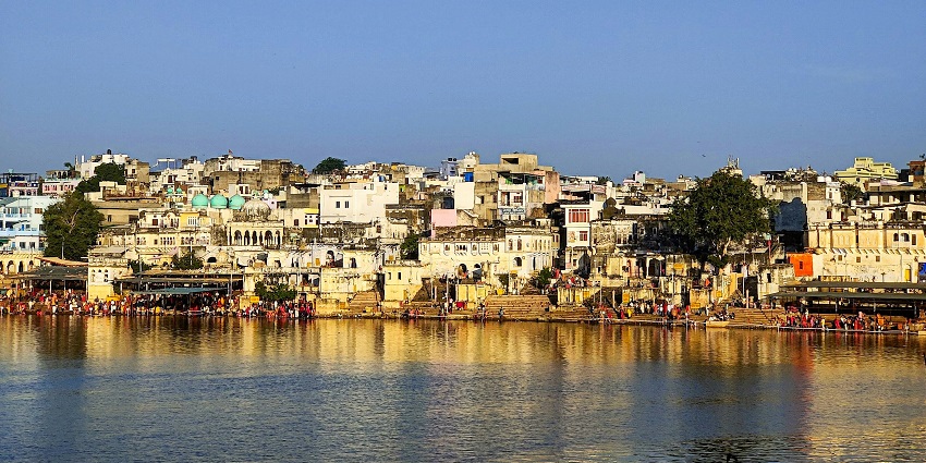 A panoramic vista of towering forts and houses surrounded by serene waters in Pushkar.