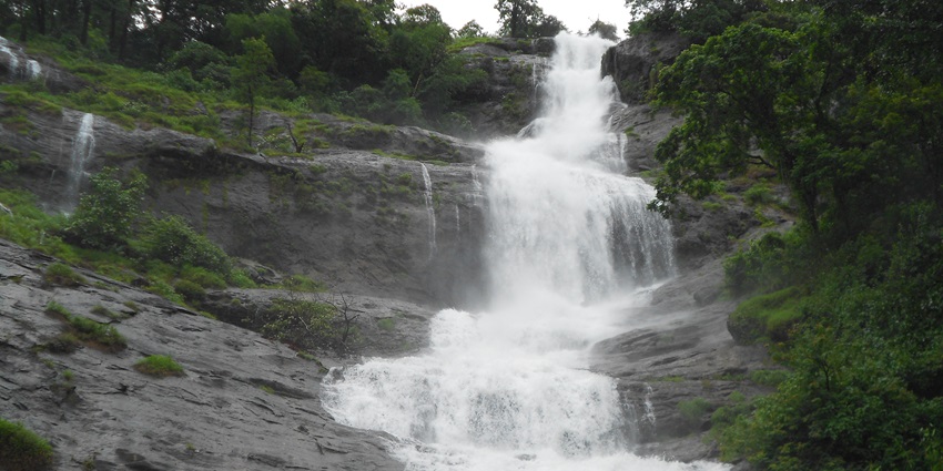 A serene cascade surrounds Putudi Waterfall in Orissa amidst a lush green and rocky landscape.