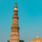 Qutub Minar, a towering ancient minaret surrounded by lush greenery and historical ruins.