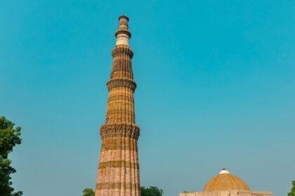 Qutub Minar, a towering ancient minaret surrounded by lush greenery and historical ruins.