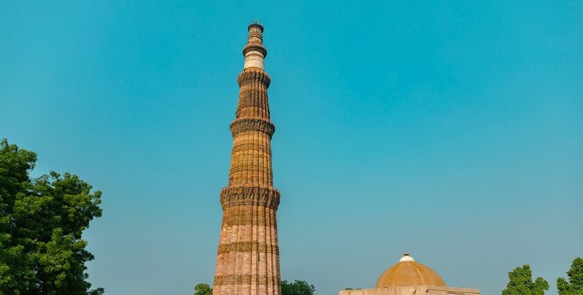 Qutub Minar, a towering ancient minaret surrounded by lush greenery and historical ruins.