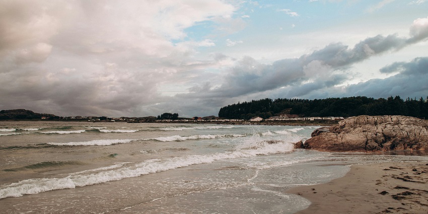A picture of a beach taken during daytime with small waves crashing at the rocky shore