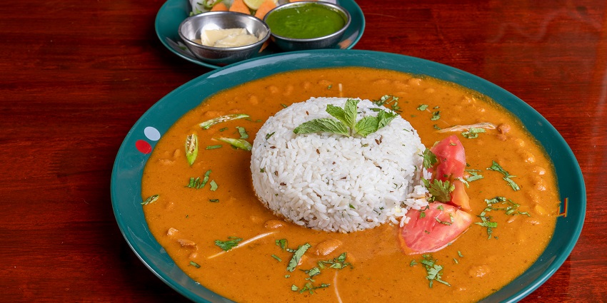 A tempting view of a green plate served with rajma rice and salad sitting on the table.
