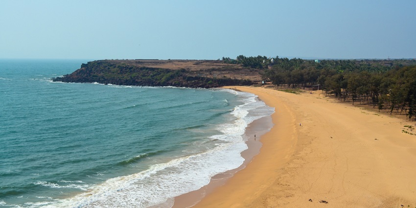 Scenic Devgad Beach with golden sand, gentle waves, and lush green backdrop.