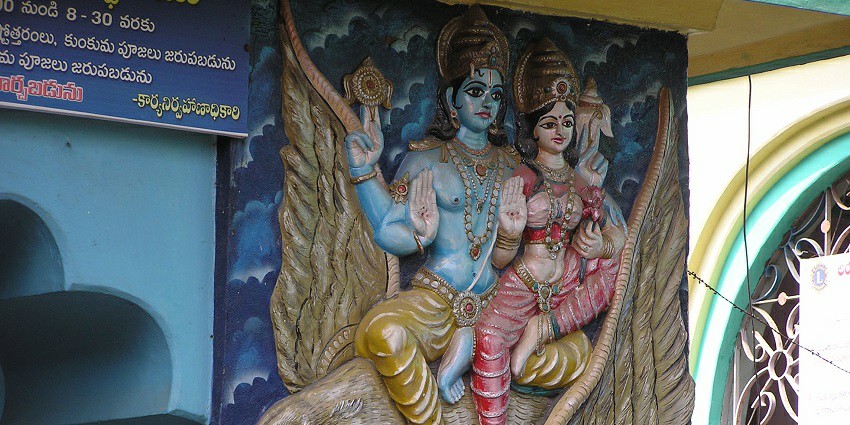 A picture of a temple wall with wall sculptures of Hindu deities sitting on a bird