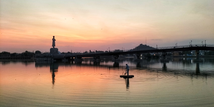 A boat on the water of Ranchi Lake with a connecting bridge and a statue along the shore