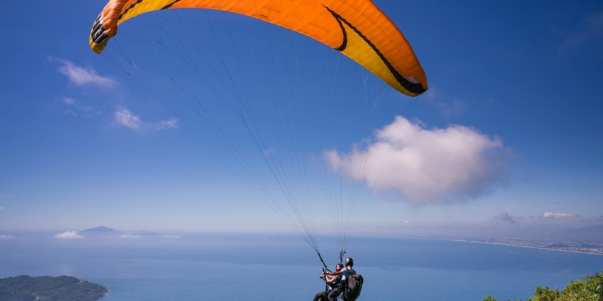 A man landing after skydiving in Pattaya with an orange, white, and blue parachute.