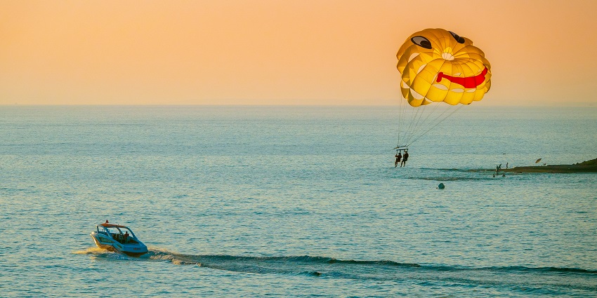 A sunset view of an azure water body with a speed boat attached to a colourful parachute.