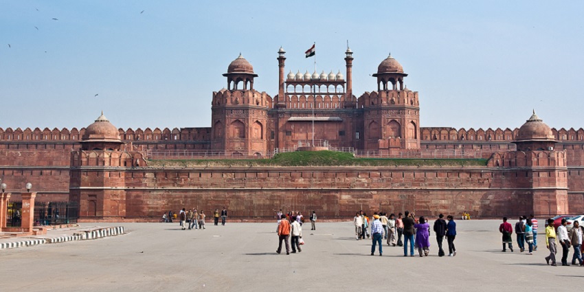 A frontal picture of a fort in Delhi with Indian Flag hoisting on the top and tourists admiring the views