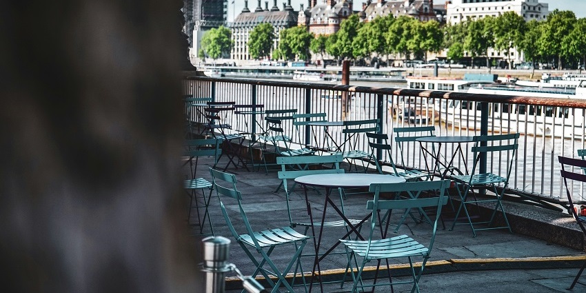 A breathtaking view of a riverside restaurant with blue chairs and tables during the day.