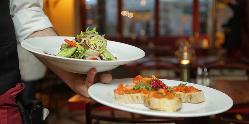 Person holding a selection of delicious pastry dishes on white ceramic plates, ready for serving.