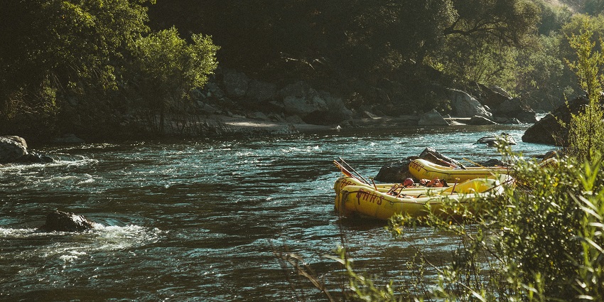 Image of rafting boats floating down the river, surrounded by lush green forest