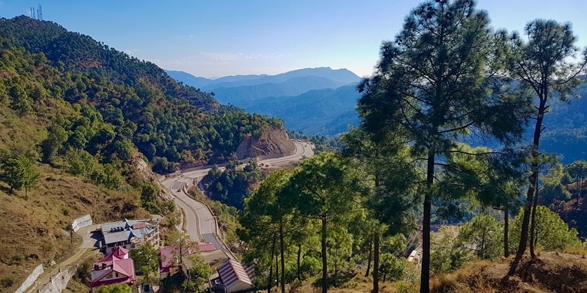 Image of beautiful lush green mountains and small local houses on side it’s twisty road