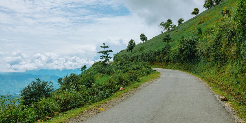 Image of winding road on a hillside surrounded by lush green grass and rolling hills.