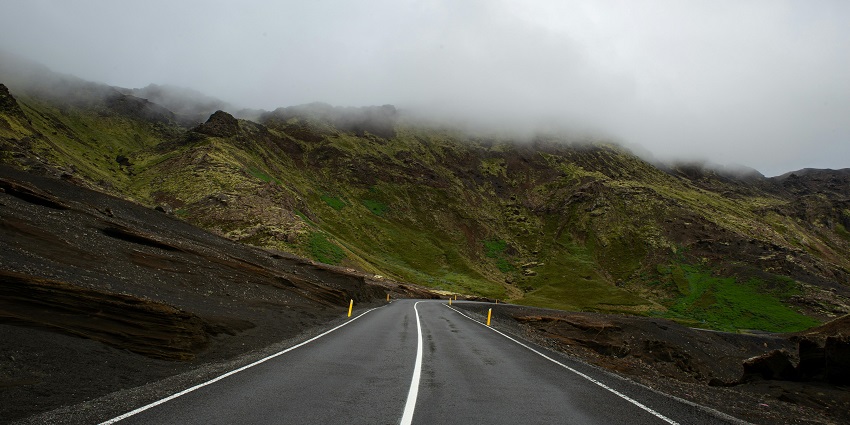 Serene empty road winding through majestic mountains under a clear blue sky.