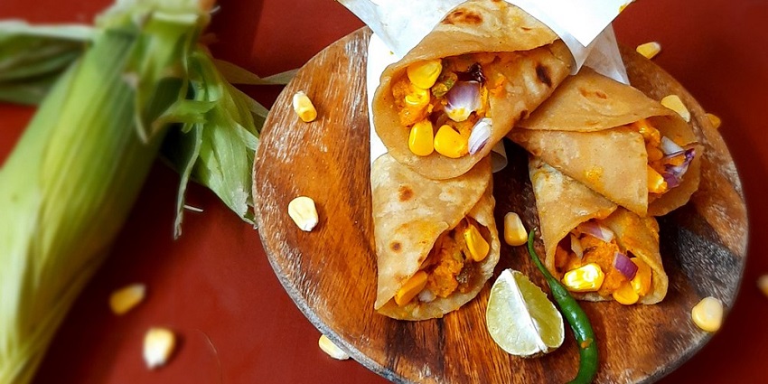A delicious view of a plate served with a kathi roll stuffed with potatoes and corns.