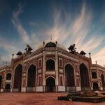 An image of a brown and black Mosque under a white and blue cloudy sky near Delhi.