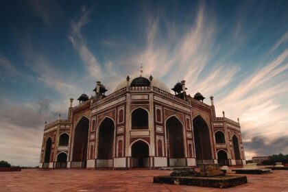 An image of a brown and black Mosque under a white and blue cloudy sky near Delhi.