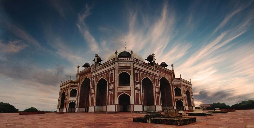 An image of a brown and black Mosque under a white and blue cloudy sky near Delhi.