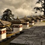 Traditional Bhutanese architecture with a stupa and mountains in the background.